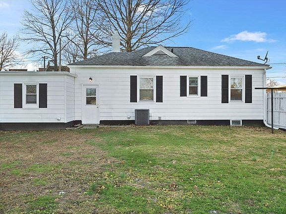 A white house with black shutters is sitting on top of a lush green field.
