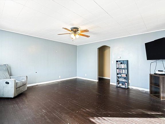 A living room with a couch , chair , television and ceiling fan.