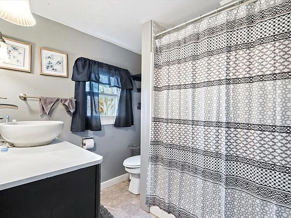 A bathroom with a sink , toilet , shower curtain and window.