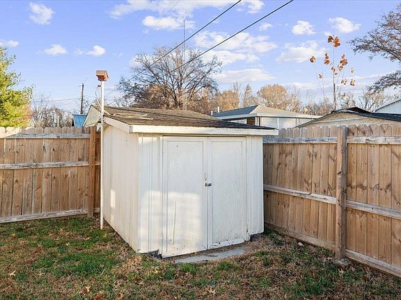 A white shed is sitting in the backyard next to a wooden fence.