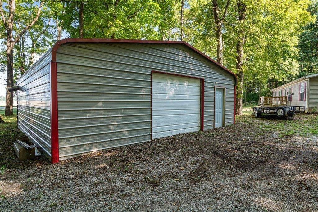 A metal garage with a red trim is sitting on top of a gravel lot.