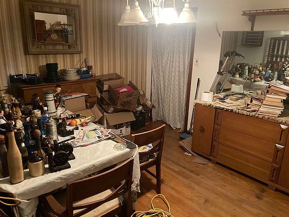 A messy dining room with a table , chairs , dresser , and mirror.