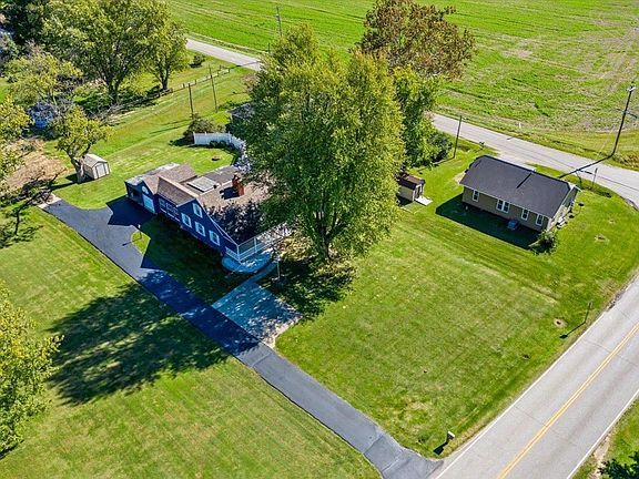 An aerial view of a house on a lush green field next to a road.