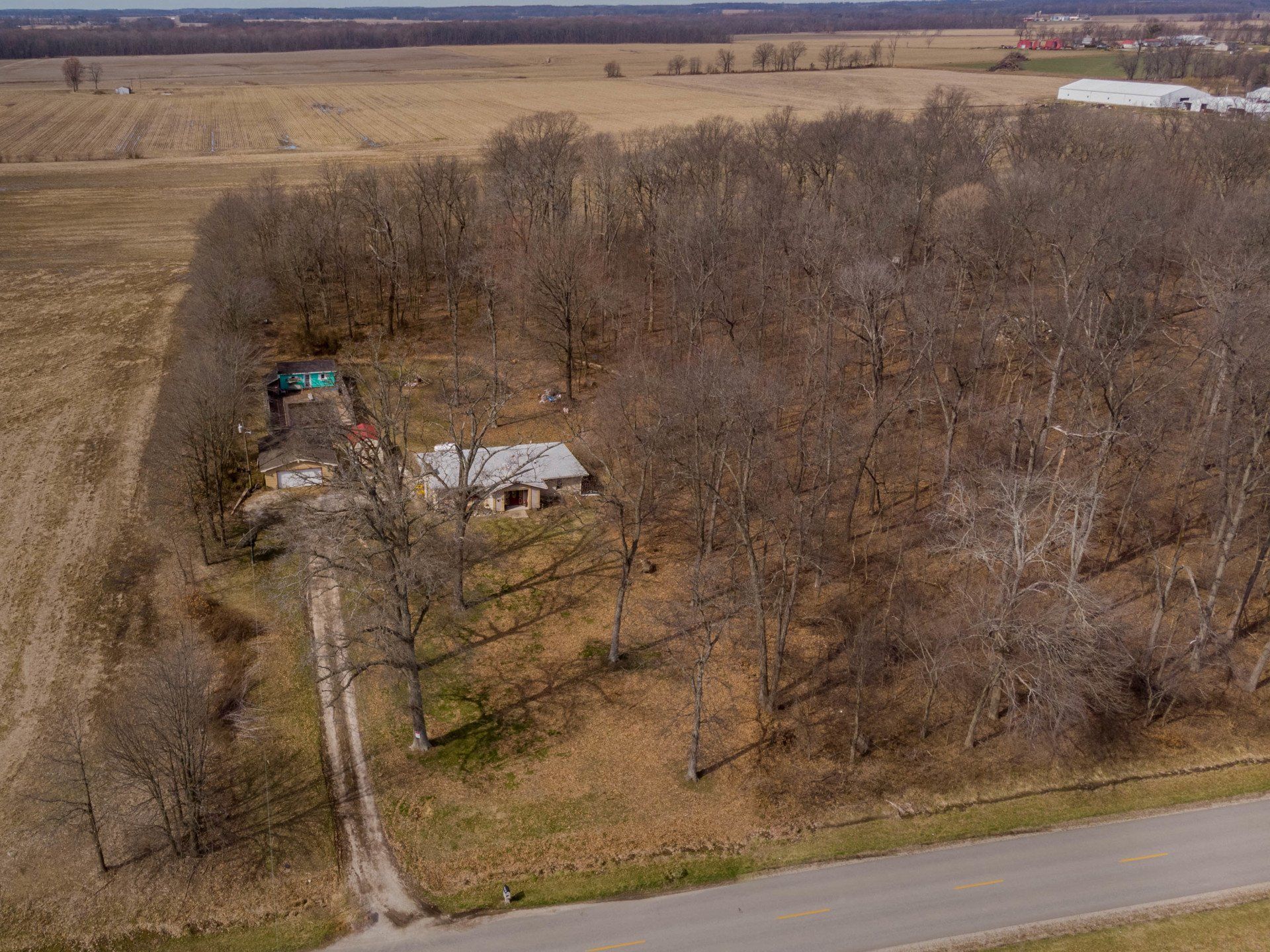 An aerial view of a house in the middle of a field surrounded by trees.