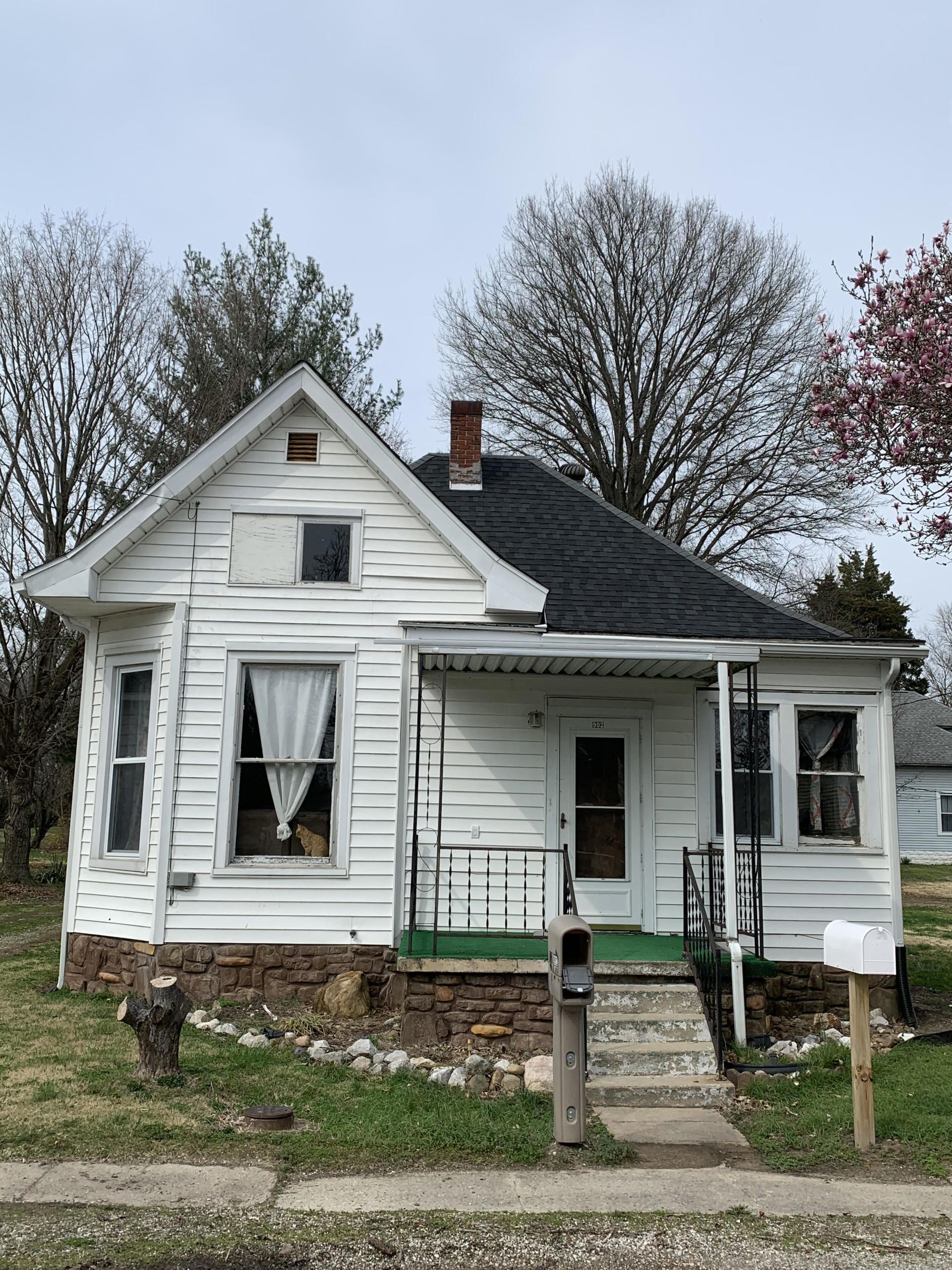 A small white house with a black roof and a mailbox in front of it.
