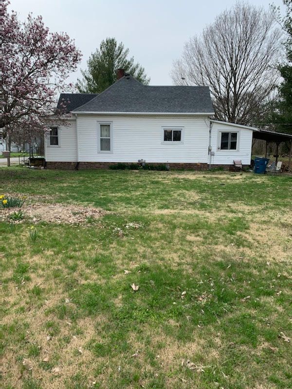 A white house with a black roof is sitting on top of a lush green field.