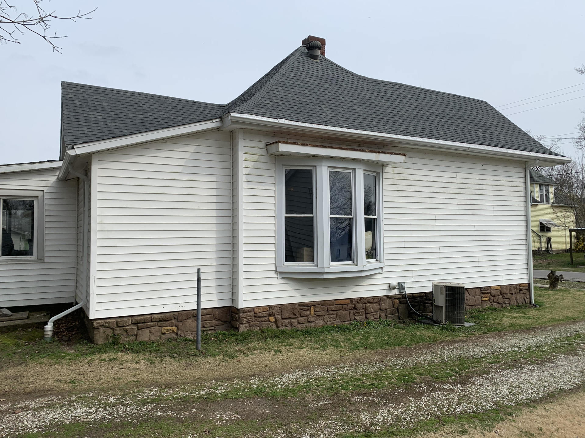 A small white house with a gray roof and a bay window.