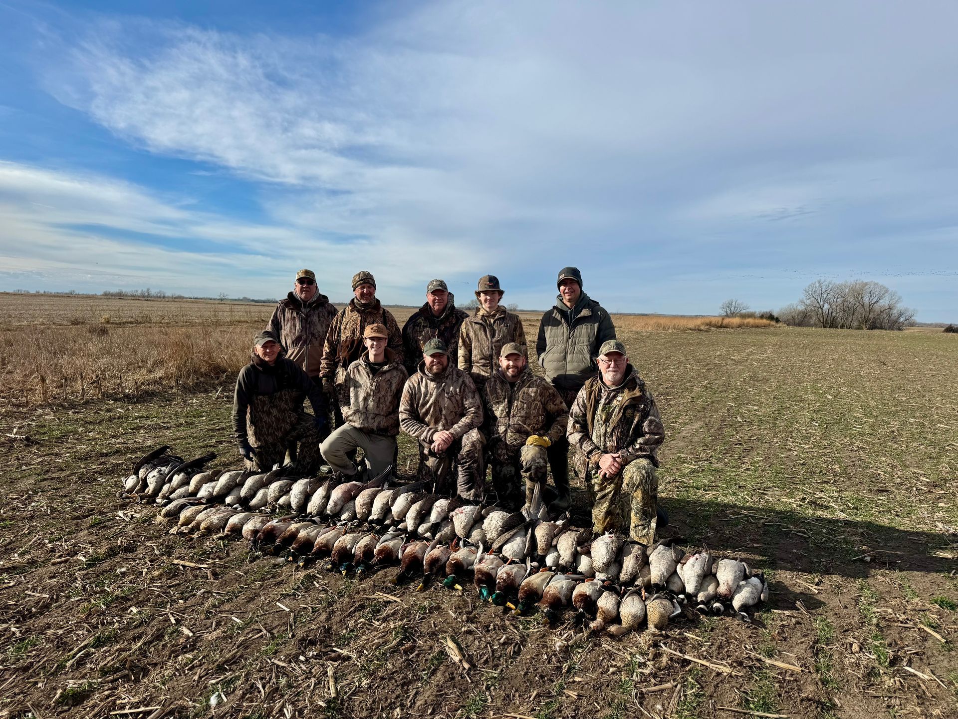 Group of hunters with harvested ducks in a field on a sunny day.