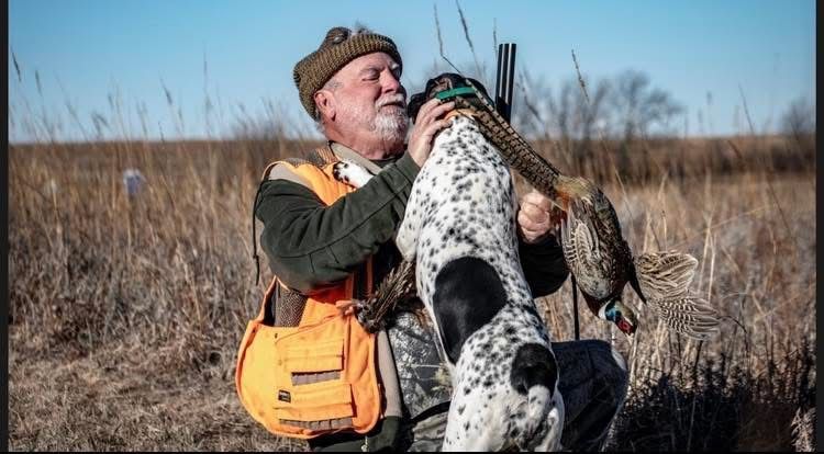 Five people in orange vests pose with hunting rifles and dead birds in a field.