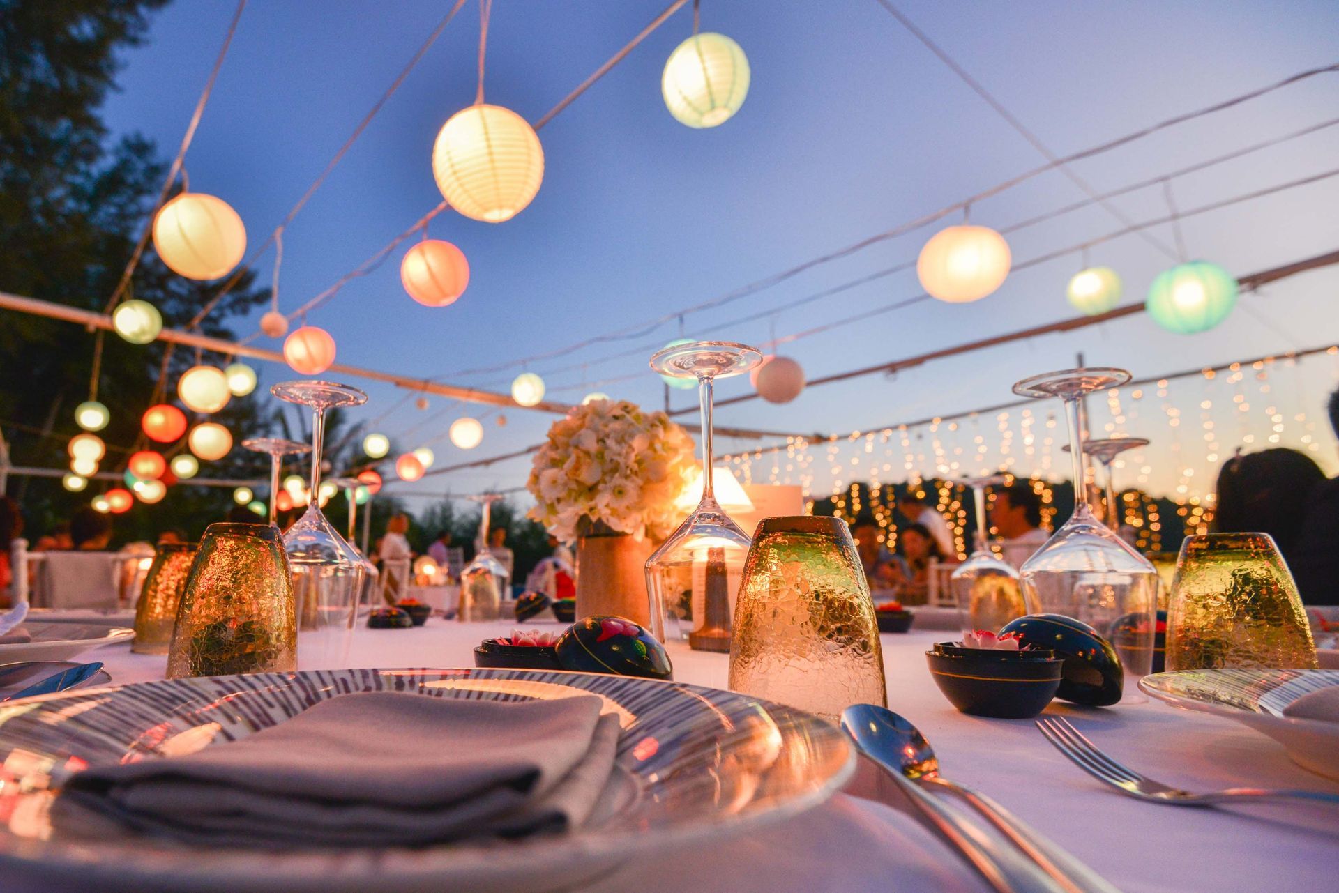 A table set for a party with plates , glasses , and lanterns hanging from the ceiling.
