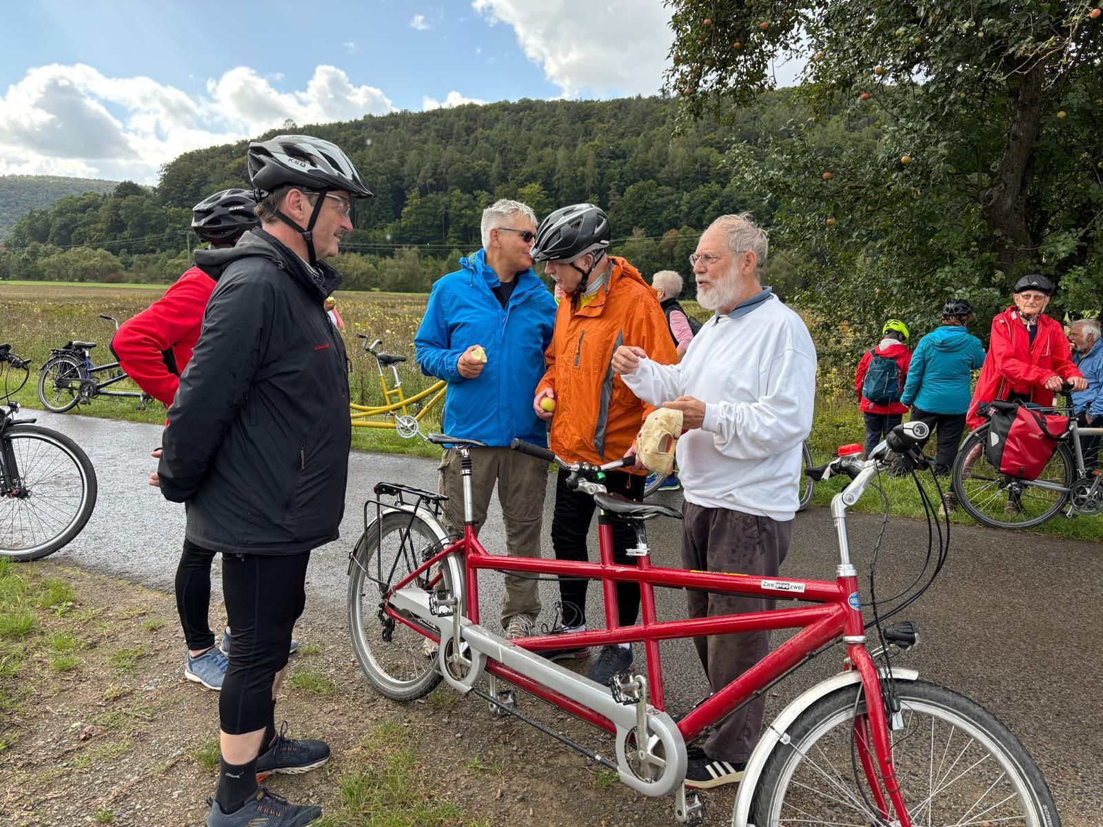 Tandem-Fahrradgruppe macht Pause auf einem Radweg in ländlicher Umgebung.