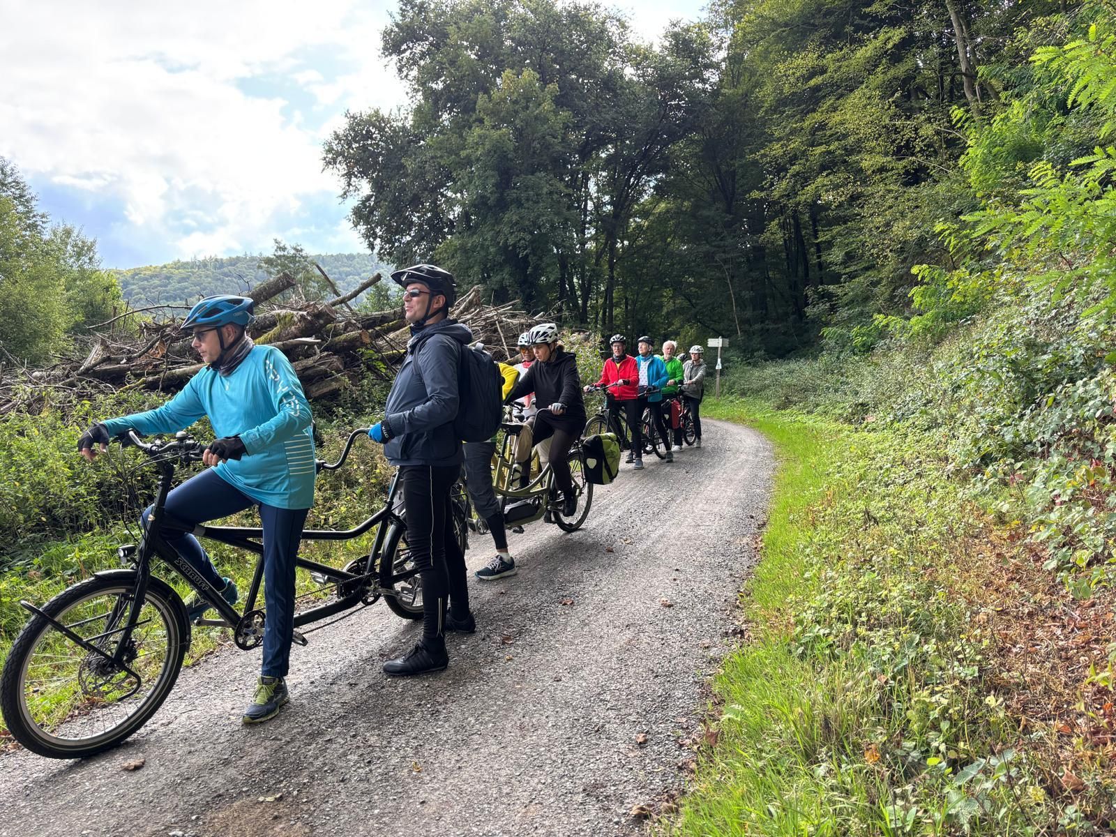 Tandem-Fahrradgruppe fährt gemeinsam auf einem Radweg durch eine Waldlandschaft.
