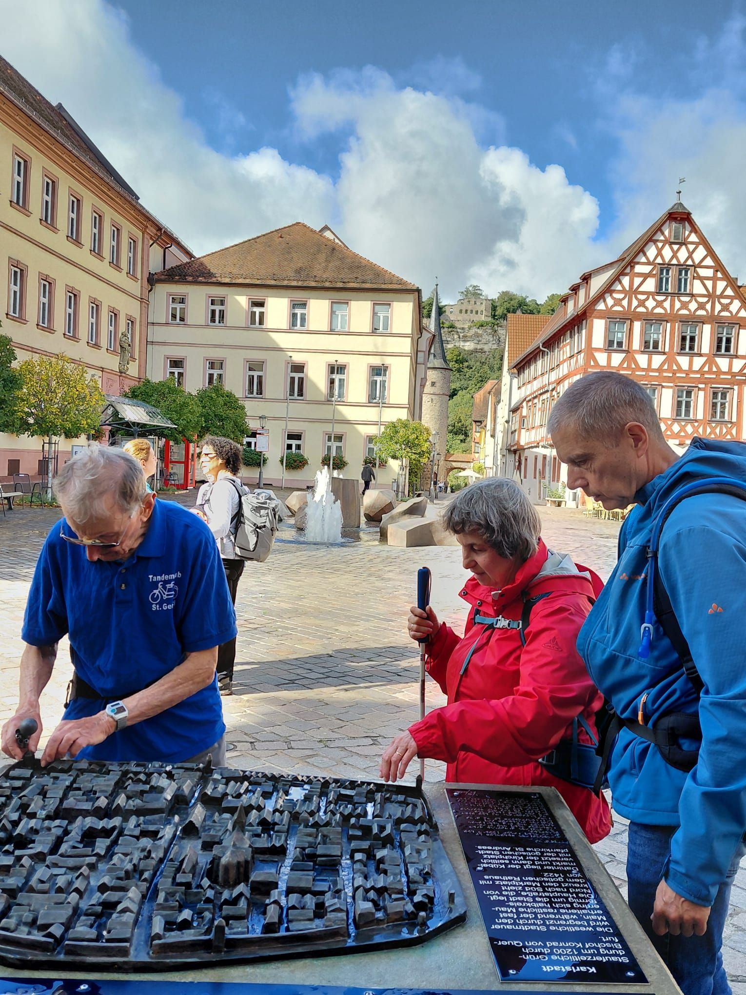 Blinde und sehbehinderte Personen erkunden ein taktiles Stadtmodell auf einem Marktplatz.
