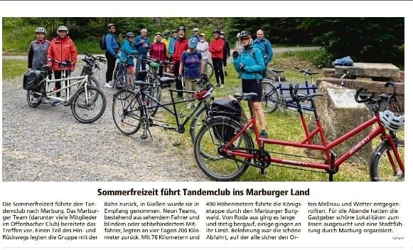 Eine Gruppe von Radfahrern des Tandemclubs Offenbach posiert mit ihren Tandemrädern auf einem Schotterweg in einer grünen Landschaft. Einige Teilnehmer tragen Fahrradhelme und bunte Sportkleidung. Im Vordergrund sind mehrere Tandemfahrräder zu sehen, während im Hintergrund Bäume und eine offene Waldlandschaft das Bild abrunden. Der Beitrag beschreibt die Sommerfreizeit des Clubs im Marburger Land.