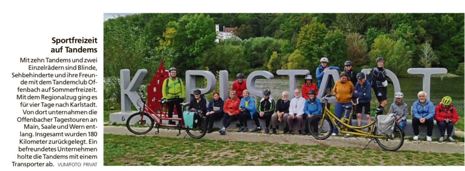 Tandem-Fahrradgruppe macht Rast vor dem Ortszeichen Karlstadt am Mainufer.