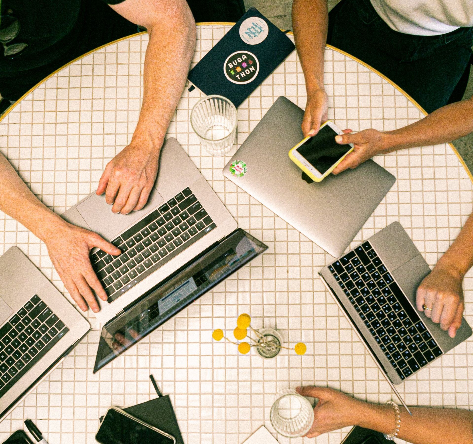 A group of people are sitting around a table with laptops and cell phones