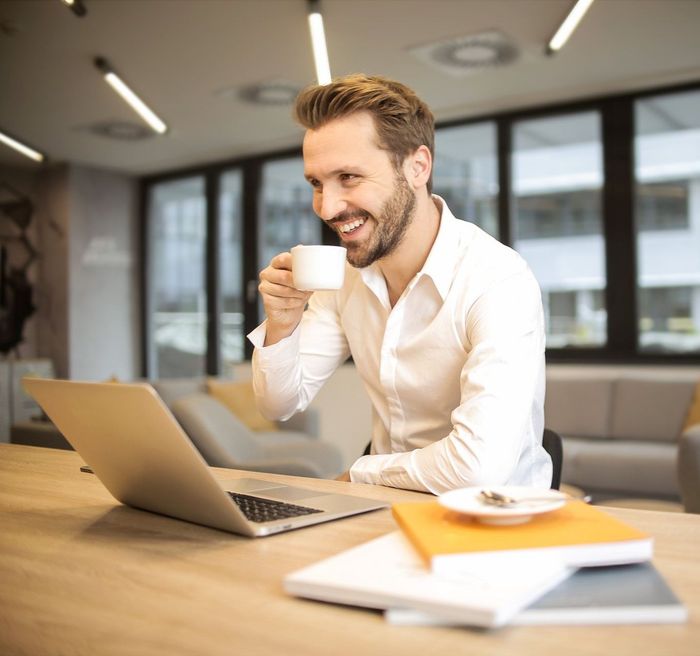 A man is drinking a cup of coffee while using a laptop