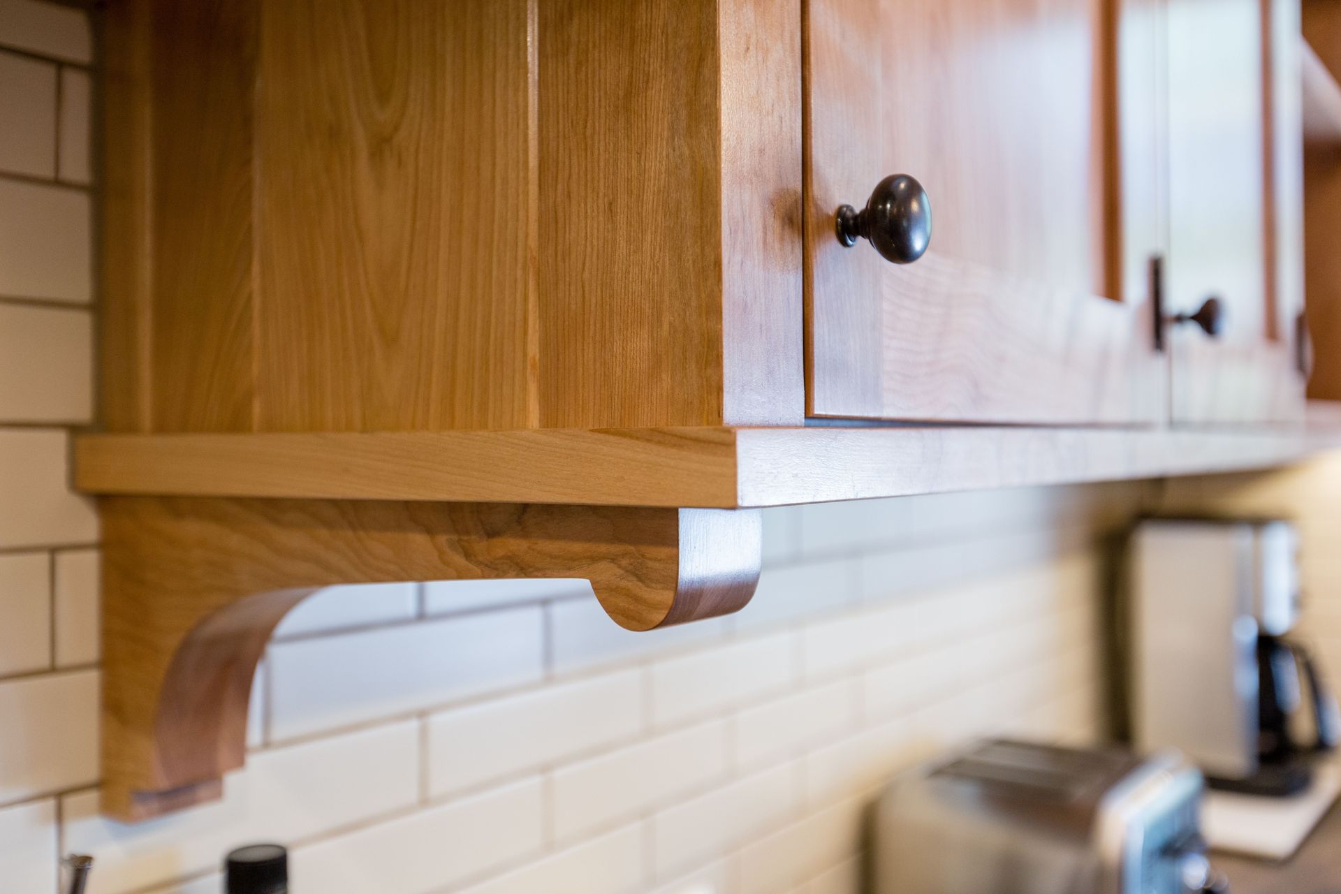 Wooden kitchen cabinets with a curved bracket above white tile backsplash.