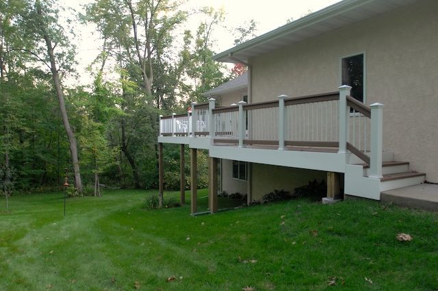 Deck on a sloped lawn next to a house with trees in the background.