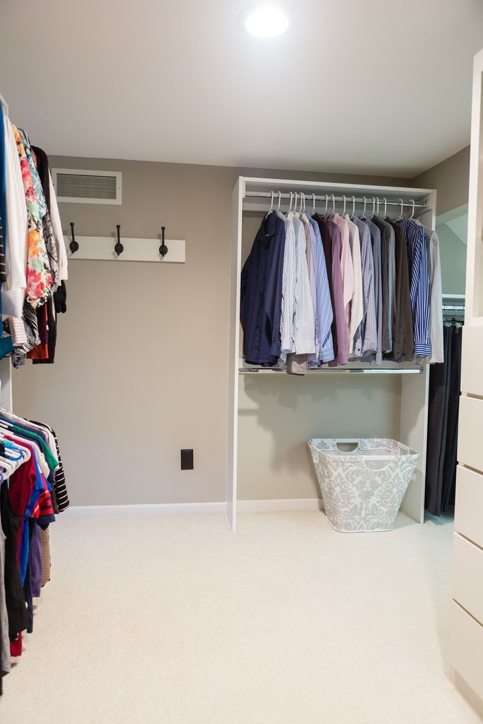 Walk-in closet with clothes hanging on racks. Beige walls, white shelving, and a basket on the floor.