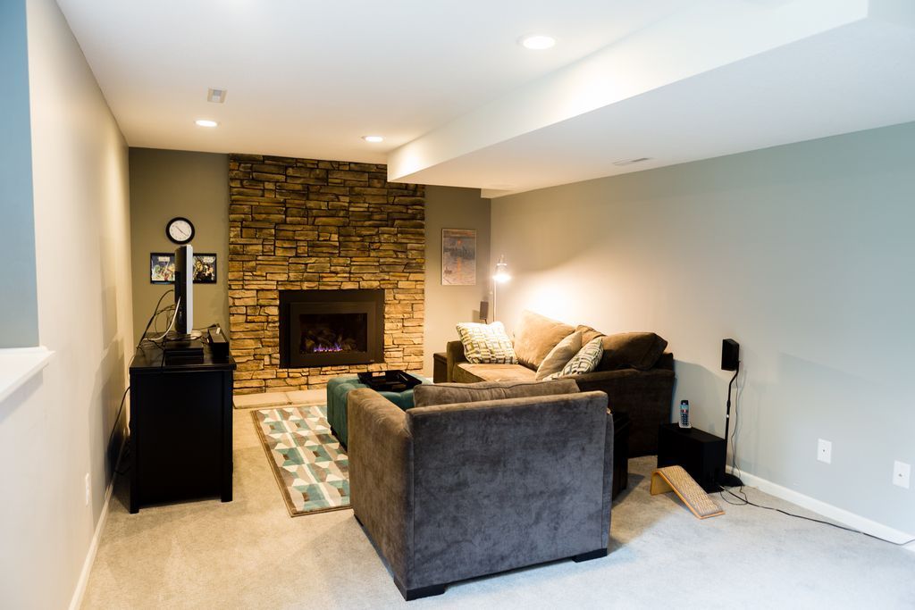 Cozy basement living room with stone fireplace, couches, and carpet.