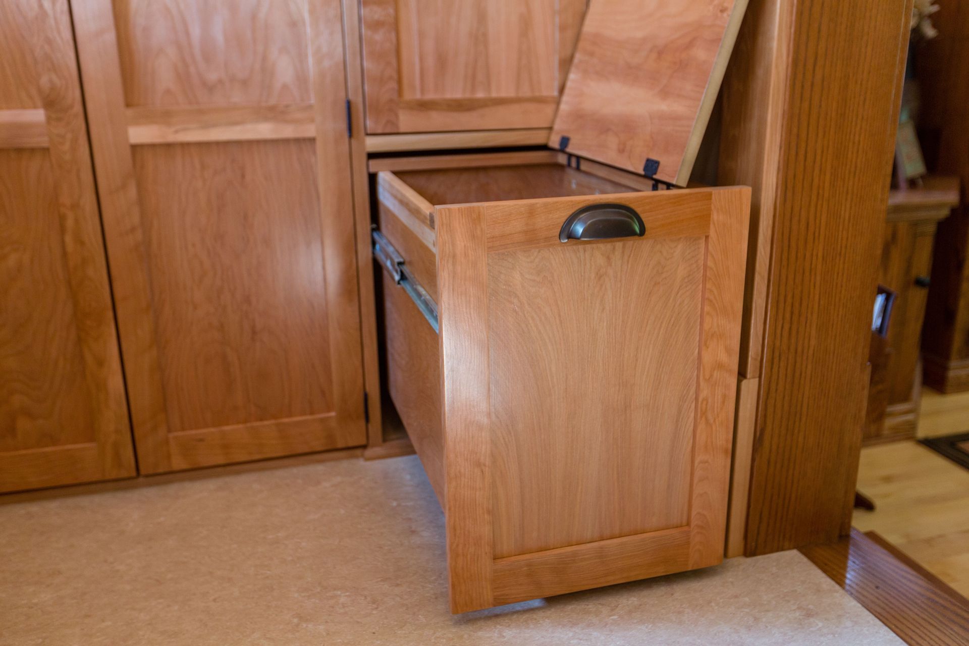 Wooden pull-out drawer with an open lid, part of a built-in cabinet in a room with beige carpet.