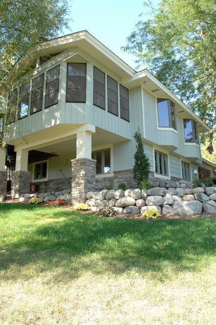 Two-story light green house with stone accents and screened porch, set on a grassy lawn.