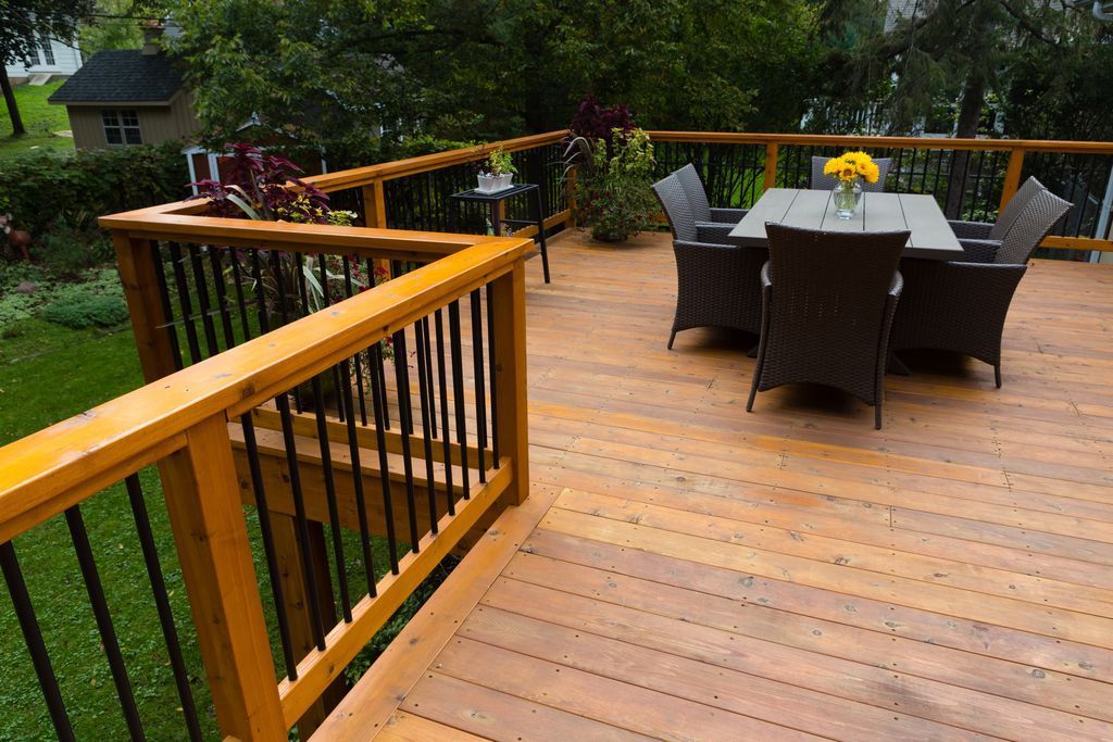 Wooden deck with black railings, a table and chairs, and a backyard.