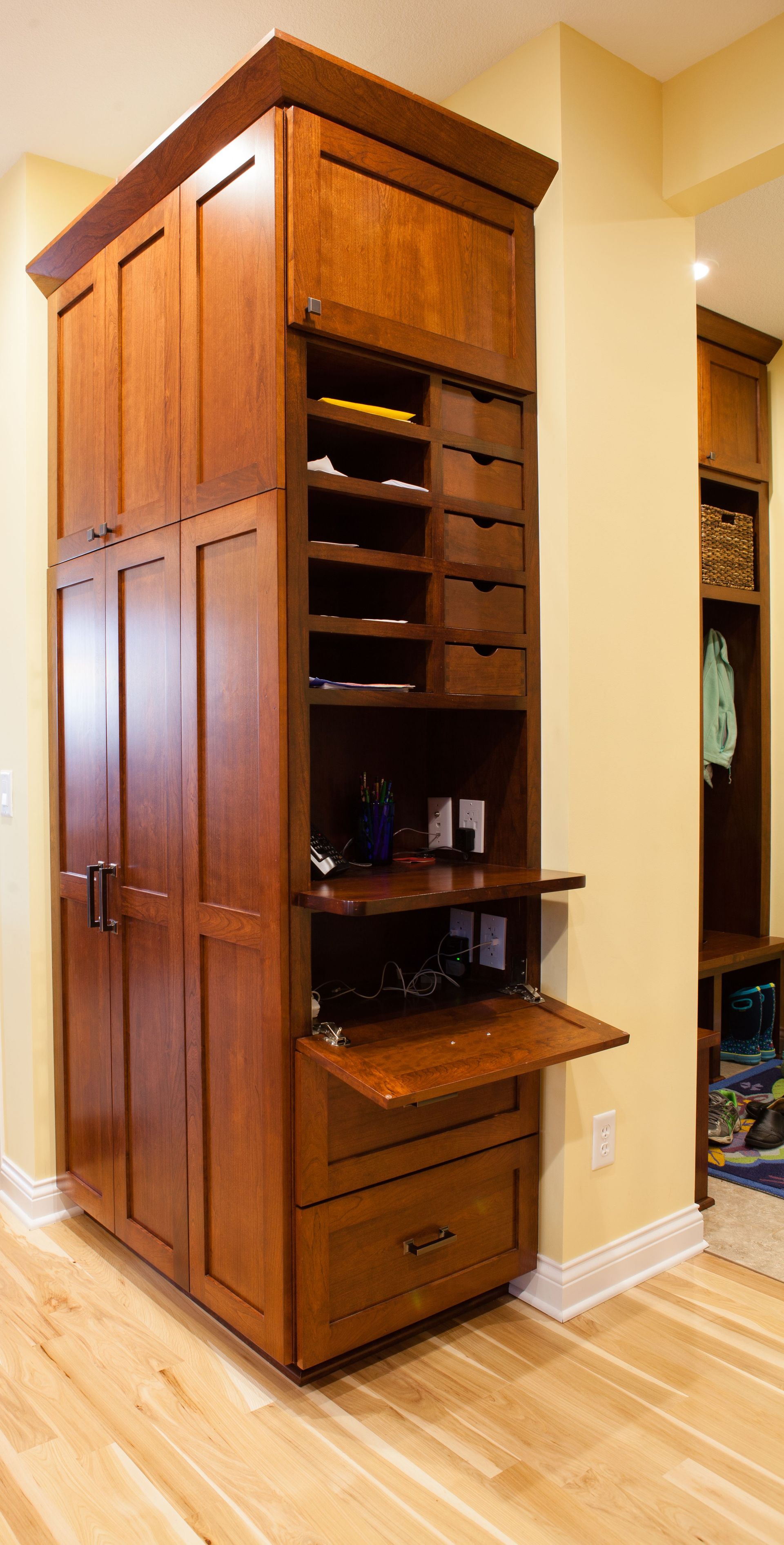 Tall, wooden closet with open sections, drawers, and shelves against a yellow wall, with light wooden floor.