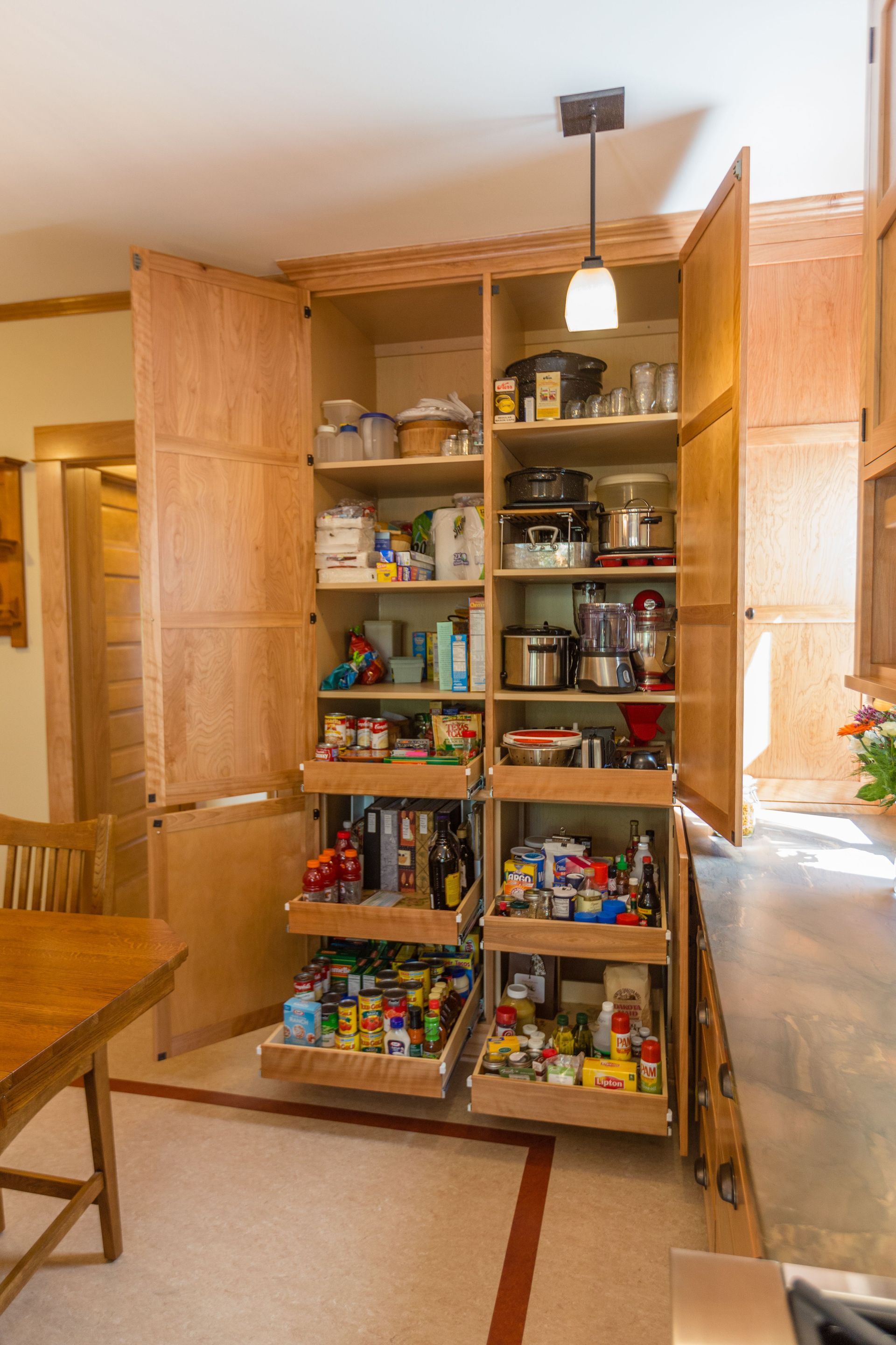 Large pantry cabinet open, revealing shelves and pull-out drawers stocked with food and appliances.