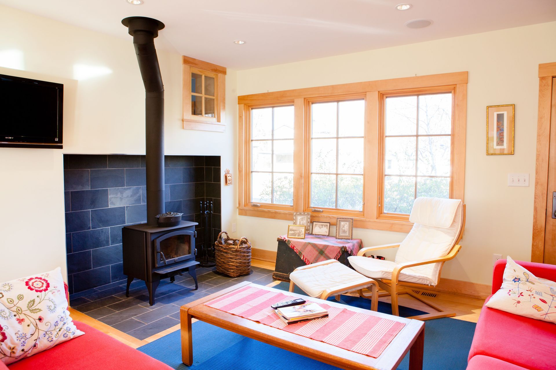 Cozy living room with a wood-burning stove, red sofa, and large windows with natural light.