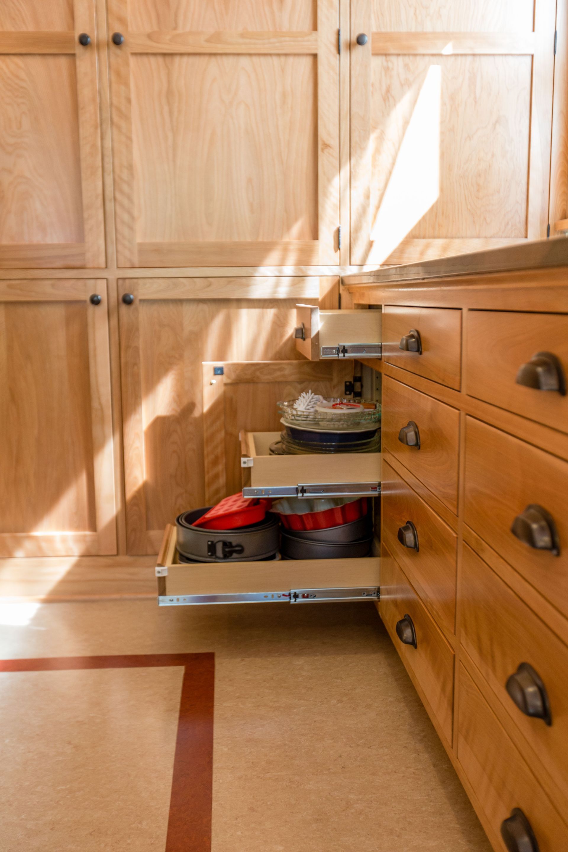 Pull-out corner cabinet with stacked shelves holding cookware in a wood kitchen.