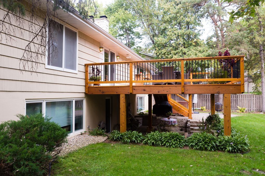 Backyard with a two-story house, wooden deck, green lawn, and foliage.