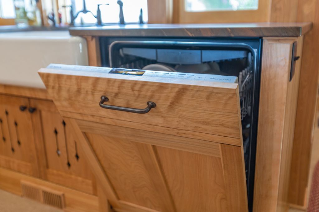 Dishwasher with wooden facade, open, revealing interior with dishes. Kitchen setting.