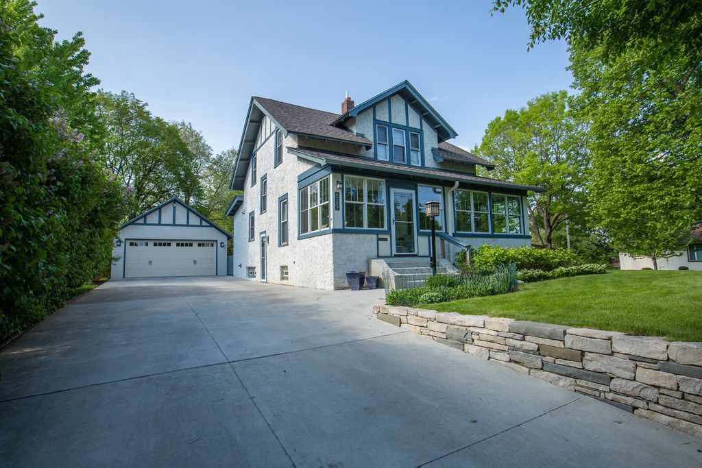 Two-story white house with a garage and long driveway. Blue trim. Green trees and grass.
