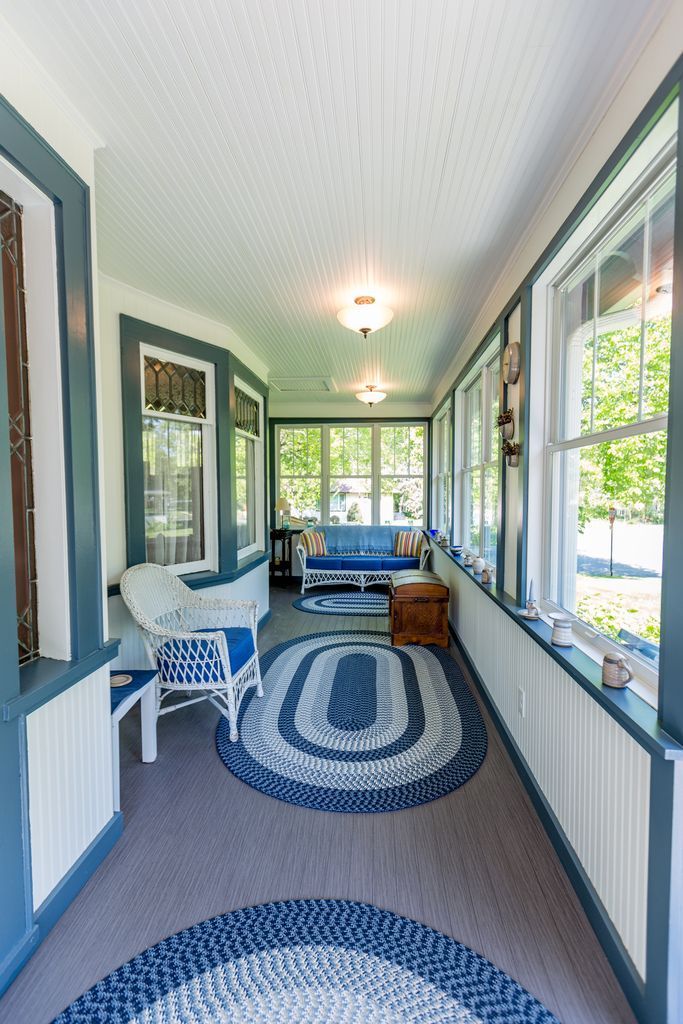 Blue and white porch with rug, wicker chair, and sofa, bright with windows and natural light.