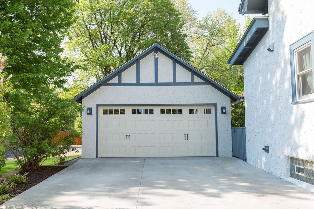 Two-car garage with light-colored door, gray trim, and concrete driveway, next to a stucco house.