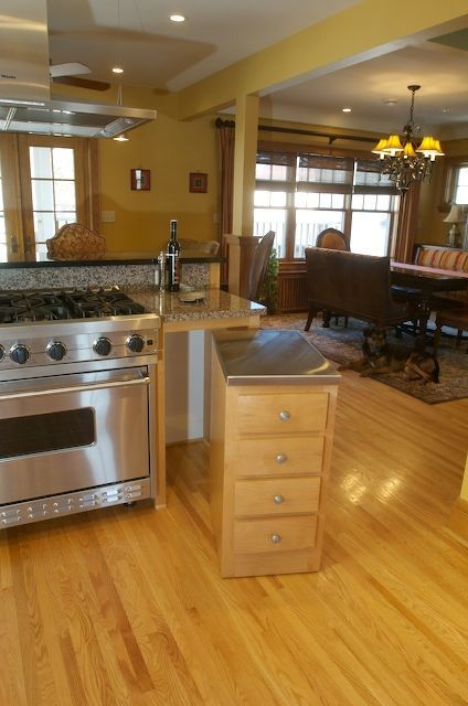 Kitchen with stainless steel appliances, light wood cabinets and floors, open to a dining area.