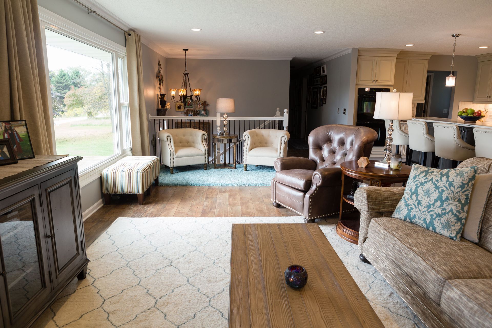 Living room with beige furniture, blue rug, large window, and open kitchen.