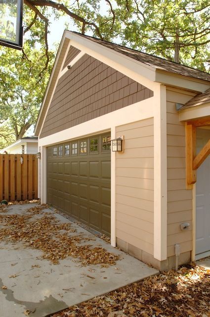 Tan-sided garage with brown shingle roof, green garage door, and concrete driveway; leaves on the ground.