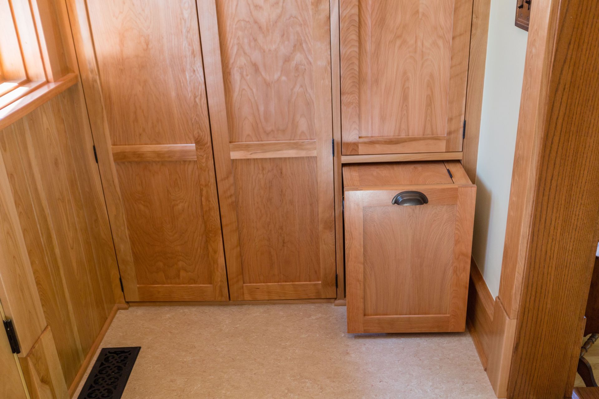 Wooden closet with a pull-out hamper, set against light wood paneling in a room.
