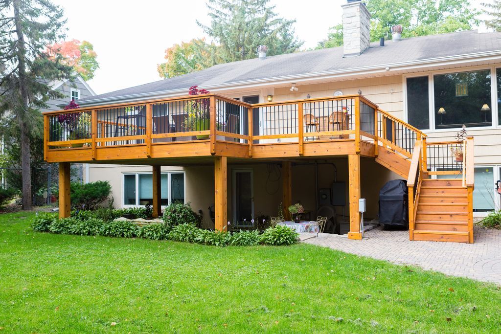 Two-level wooden deck attached to a beige house with green grass in front.
