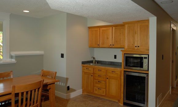 A basement kitchen area with wooden cabinets, a microwave, sink, and mini-fridge; light green walls.