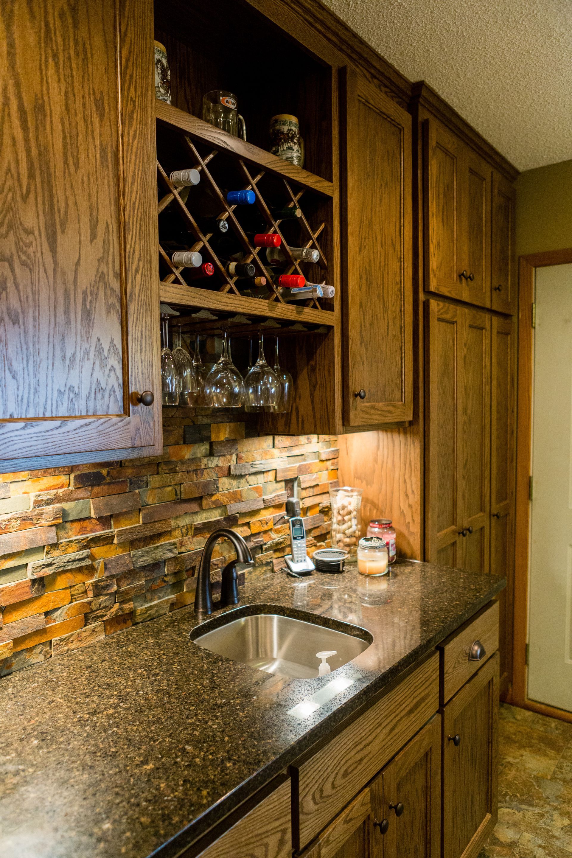 Wet bar with dark wood cabinets, stone backsplash, and wine storage.