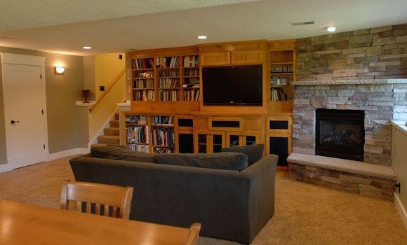 A finished basement with built-in shelves, TV, and fireplace, furnished with a sofa and table.
