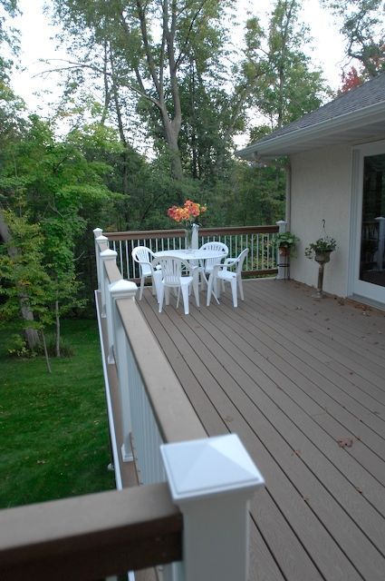 Wooden deck with white furniture, overlooking a green yard and trees.