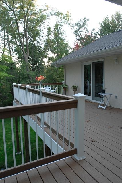 Deck with white railings, brown handrails, and a sliding glass door. Lawn and trees in the background.