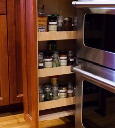 Spice rack pull-out cabinet beside an oven. Wooden cabinet with jars of spices visible.