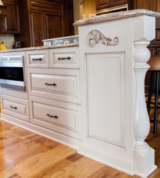 Cream-colored kitchen island with decorative details, drawers, and a microwave, on a wooden floor.