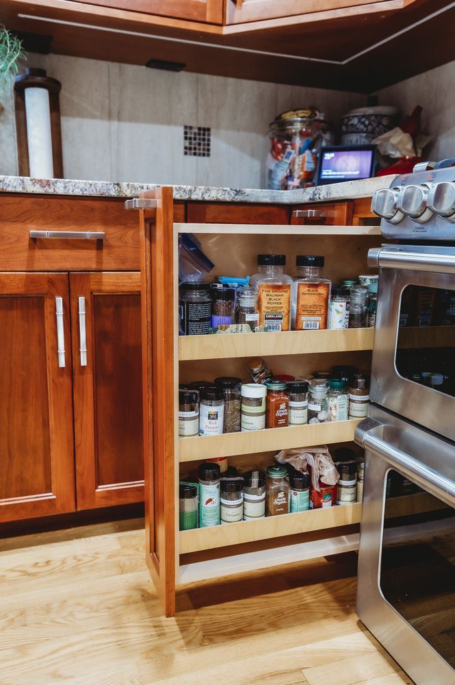 Pull-out spice rack in a kitchen next to a stainless steel stove, stocked with various spice containers.